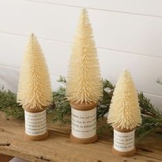 three small white christmas trees sitting on top of a wooden table next to each other