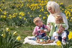 a woman and two children sitting on a blanket in the grass with yellow daffodils