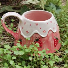 a red and white ceramic mug sitting on the ground next to some green plants with hearts painted on it