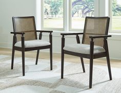 two chairs sitting on top of a white rug in front of a window with large windows