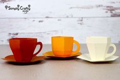 three different colored cups and saucers sitting on top of a wooden table next to each other