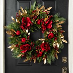 a christmas wreath with red flowers and greenery hangs on a black front door,