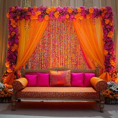 an orange and pink wedding stage with flowers on the wall, couches and drapes