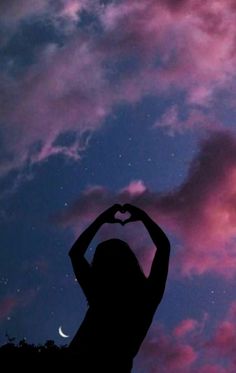 the silhouette of a woman making a heart shape with her hands against a night sky