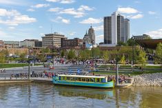 a blue and white boat floating on top of a river next to a city filled with tall buildings