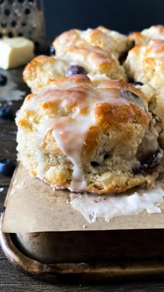 blueberry muffins with icing sitting on top of a cutting board