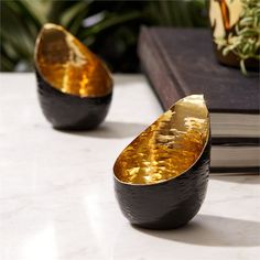 two gold and black vases sitting on top of a table next to a book