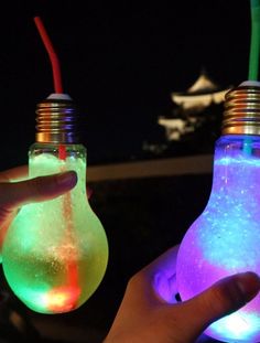 two light bulbs that have been turned on with different colored lights inside them, and one being held in the air by someone's hand