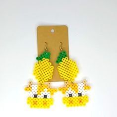 the earrings are made out of yellow and white beads with green leaves on them, sitting next to a card