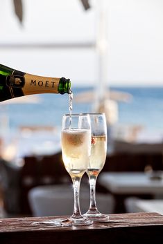 champagne being poured into two wine glasses on a table at an outdoor restaurant overlooking the ocean