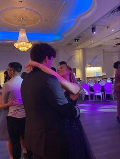 two people hugging each other while standing in a room with purple lights on the ceiling