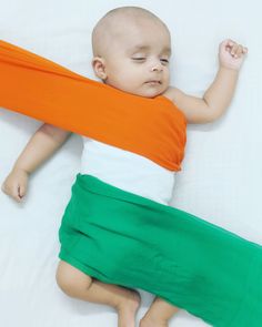 a baby laying on top of a bed wearing an orange and white blanket over it's back