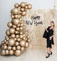 a woman standing in front of a backdrop with gold balloons and the words happy new year written on it