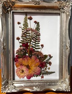 a silver frame with flowers in it sitting on a table