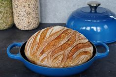 a loaf of bread sitting in a blue skillet on a counter next to some jars