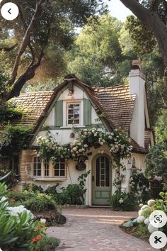 a white house with green shutters and flowers on the front door is surrounded by greenery