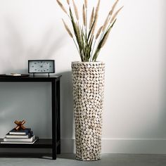 a tall vase sitting on top of a table next to a clock and some books