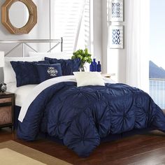 a bed with blue comforters and pillows in a room next to a window overlooking the ocean