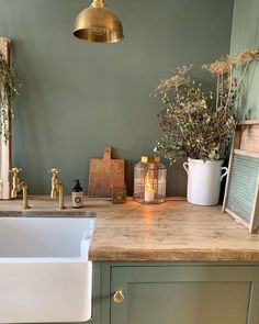 a kitchen with green walls and white sink, gold faucet, wooden cutting board on the counter