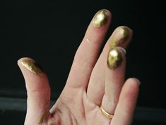 a woman's hand with gold nail polish on it and her fingers in the air