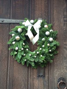 a green wreath with white ornaments hanging on a door