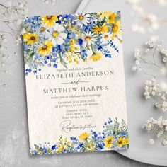 a wedding card with yellow and blue flowers on it next to some baby's breath