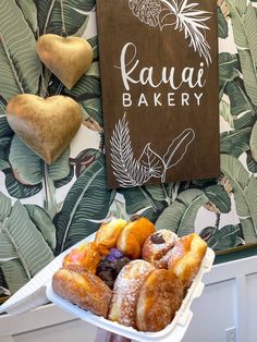 a person holding a tray of doughnuts in front of a sign that says kauai bakery