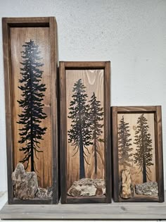 three framed pictures with trees on them sitting on a shelf next to rocks and stones