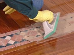 a person in yellow gloves and rubber gloves cleaning a wooden floor