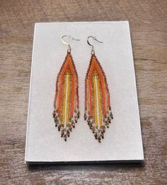 These earrings are handmade with Japanese myuki beads and accent beads on the ends of the fringe. The colors include various shades of orange, cream white and brown. Artisan Brown Beaded Fringe Earrings, Handmade Orange Teardrop Beaded Earrings, Brown Beaded Earrings With Fringe, Orange Teardrop Beaded Earrings With Ear Wire, Orange Teardrop Beaded Earrings With Dangling Beads, Orange Fringe Dangle Earrings, Handmade Orange Long Drop Earrings, Handwoven Orange Beaded Earrings For Gift, Traditional Brown Beaded Fringe Earrings