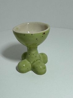 a green ceramic bowl with two legs on a white surface