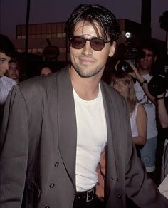 a man wearing sunglasses and a suit walking in front of a group of people at an event