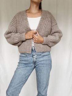 a woman standing in front of a white backdrop wearing a sweater and jeans with her hands on her hips