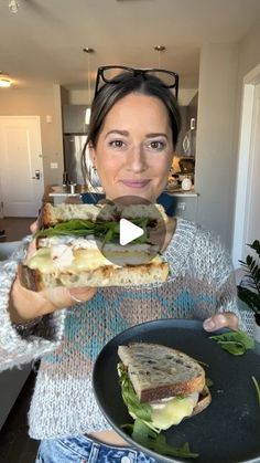 a woman holding a sandwich in her hand and looking at the camera with an excited look on her face