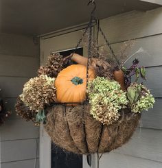 a hanging basket filled with pumpkins and other fall decorations on the front door of a house