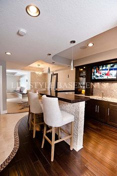 a large kitchen with wooden floors and white bar stools in front of the counter