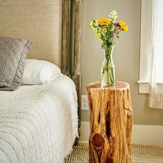 a vase with flowers sitting on top of a wooden table next to a white bed