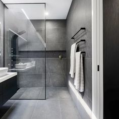 a modern bathroom with black and white fixtures, glass shower doors, gray tile flooring