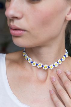 a woman wearing a necklace with yellow and blue flowers on the front, while holding her hand up to her chest