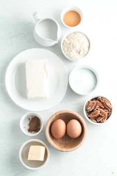 the ingredients to make pecan pie laid out on a white tablecloth, including eggs, flour, butter, and sugar