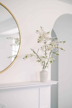 a vase filled with flowers sitting on top of a white mantle next to a mirror