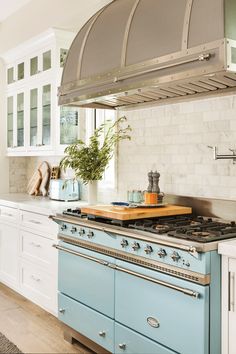 a blue stove top oven sitting inside of a kitchen next to white cabinets and drawers