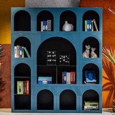 a blue book shelf with books on it next to potted plants and vases