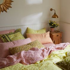 a bed covered in pink and yellow sheets next to a dresser with flowers on it