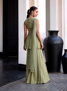 Step into enchanting sophistication with this sage green shimmer georgette peplum ensemble! Embellished with intricate checks embroidery in cut-daana and sequins, it exudes timeless charm and elegance. The attached net drape adorned with handmade tassels adds a touch of grace and movement. Paired with sharara pants, this ensemble offers a perfect balance of tradition and contemporary flair. Sharara Pants, Sharara Set, Sage Green, Checks, Green