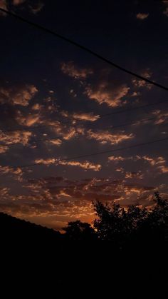 the sun is setting behind some clouds in the sky above trees and power lines on a hill