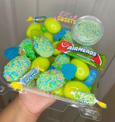 a hand holding a container filled with green and blue sprinkle covered donuts