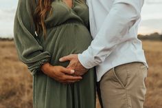 a pregnant couple holding hands while standing in a field