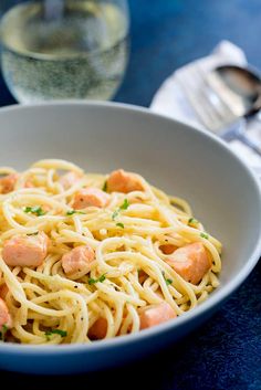 pasta with shrimp and parsley in a white bowl on a blue tablecloth next to a glass of water