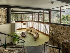 a living room filled with lots of furniture next to a stone wall covered in windows